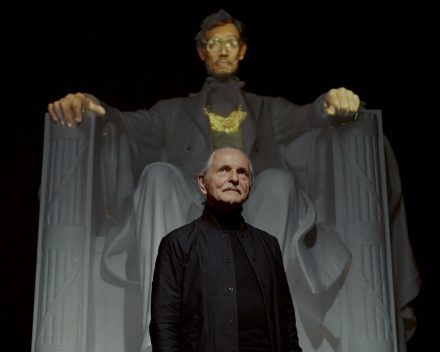 The artist Krzysztof Wodiczko at Galerie Lelong, next to a replica of the statue in the Lincoln Memorial. A video projects the faces and hands of Staten Island residents. Credit: Vincent Tullo for The New York Times 